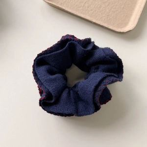 Dark blue knitted scrunchie with red zigzag stitching on a neutral surface