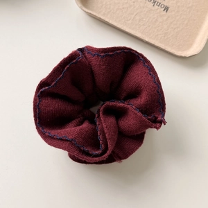 Detailed texture of dark red knit scrunchie with contrast blue wavy stitched edges