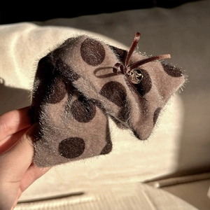 Détail d'une pince à cheveux en peluche à pois avec nœud brun et pendentif doré