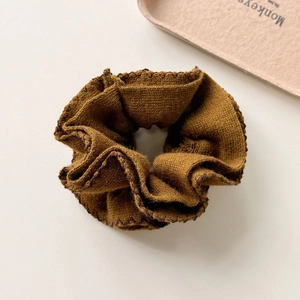 Detailed view of a brown knitted scrunchie with soft ribbed texture and wavy edges