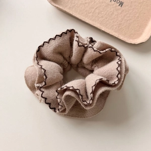 Macro detail of beige knitted scrunchie with brown wavy stitching and soft fabric texture