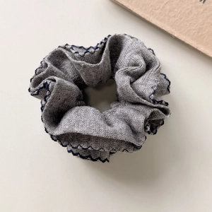 Detailed close-up of a grey knitted scrunchie with elegant navy blue wavy edge finish