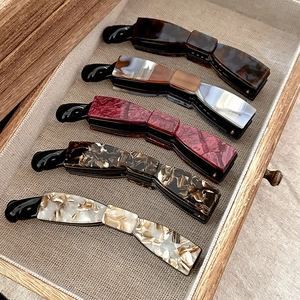 Assorted acetate banana hair clips with tortoiseshell and marble patterns in a wooden tray