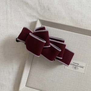 Detailed texture of burgundy velvet bow hair clip with lilac piping on gray tray