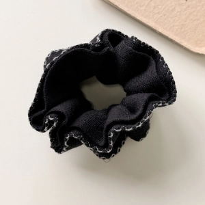Detail of black knitted scrunchie with white contrast stitching and wavy edge finish