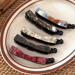 Five assorted resin banana hair clips with marble texture patterns on ceramic tray