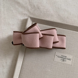 Detail of pink wool bow banana clip with dark brown edges on textured tray