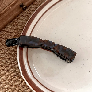 Dark tortoiseshell bow hair clip with sleek resin finish on white ceramic plate