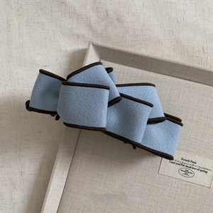 Detail view of a blue wool fabric bow banana clip with brown trim on a textured surface