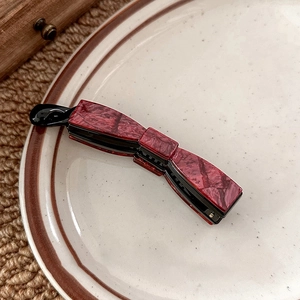 Deep red acetate banana hair clip with marble texture shown on a ceramic plate