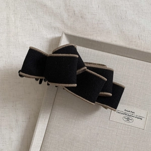 Close-up of black layered fabric bow hair clip with khaki trim detailing on a grey tray