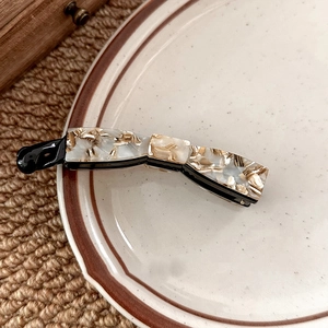 Macro detail of marble pattern banana hair clip with cream and gold textures on porcelain