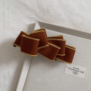 Detail of a brown multi-layered woolen bow banana clip with elegant gold wire edges