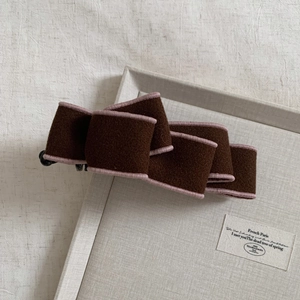 Detail of dark brown wool bow banana hair clip with light pink edging on a tray