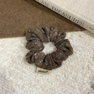 Close-up of a brown knitted scrunchie with a logo label on soft wool texture