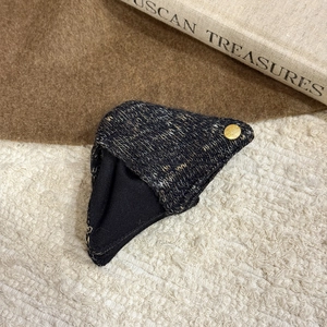 Macro shot of a dark gray knit hair clip with a gold metal label and warm cozy background