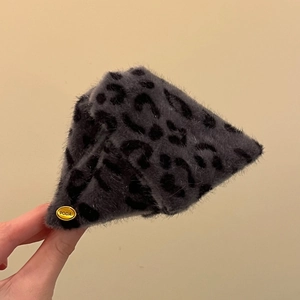 Détail d'un chapeau en peluche léopard gris avec une plaque métallique dorée PODA