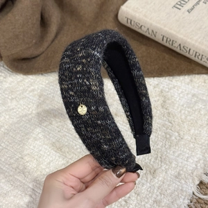 Detail of knitted wide headband in dark gray with gold logo tag and non-slip lining
