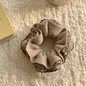 Knitted beige scrunchie with brown edging on soft white plush background