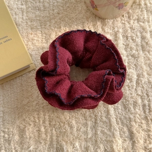 Close-up of burgundy knitted scrunchie with blue scalloped edges on soft cream background