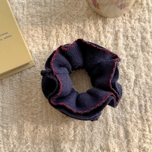 Detail of dark blue knitted scrunchie with red wavy edge stitching on soft white fabric