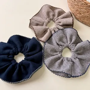 Three oversized ribbed knit scrunchies in blue, grey, and brown with wavy edge finish