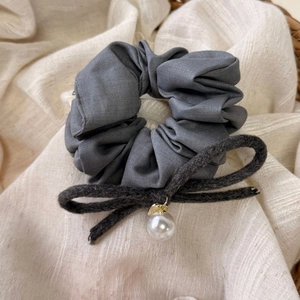 Dettaglio di scrunchie in raso grigio scuro con fiocco di peluche e pendente con perla