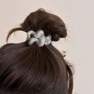 Détail d'un chouchou en peluche grise fixant un chignon brun dans un décor épuré chic