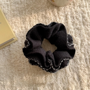 Macro shot of black knit scrunchie with white scalloped edges on soft cream fabric