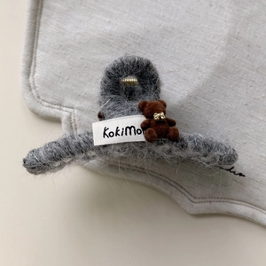 Detalle macro de una pinza para el pelo gris de felpa con un oso 3D y un lazo dorado