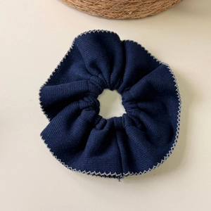 Detailed view of dark blue knitted scrunchie with contrast white wavy edge stitching