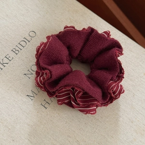 Detail of burgundy knitted scrunchie with striped ruffles on vintage book background