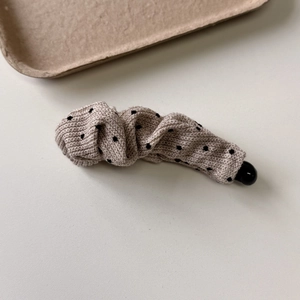 Detail of a creamy polka dot fabric banana clip with soft knitted texture and sleek black clasp