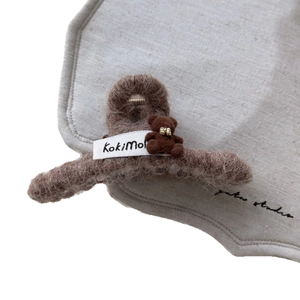 Pinza para el pelo de felpa marrón con oso decorativo y etiqueta sobre fondo de tela