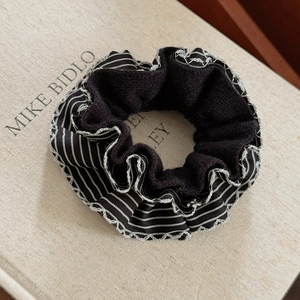 Detail shot of black knit scrunchie with striped silk-textured ruffled edges on a table