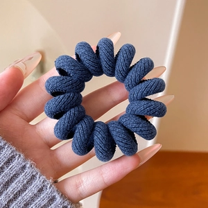 Détail d'un élastique spirale en tissu denim bleu foncé tenu à la main pour les cheveux