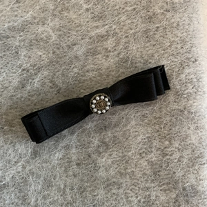 Pince à cheveux nœud en satin noir élégant avec centre en perles sur fond en peluche