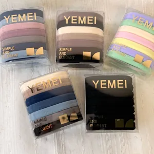 Five transparent boxes of colorful elastic hair ties on a textured cream fabric base