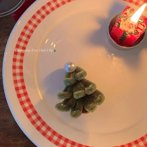Handmade plush Christmas tree hair clip with white pearl detail on a festive plate