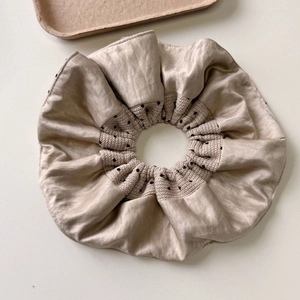 Detailed view of beige polka dot scrunchie with silk texture and knit fabric layers