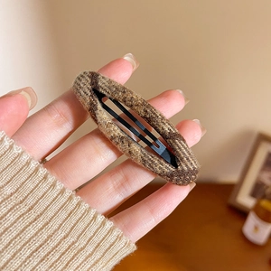 Close-up of brown tweed fabric BB hair clip held by hand showing woven texture