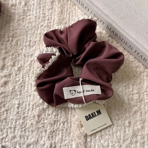 Gros plan du chouchou en tissu bordeaux avec bordure en dentelle blanche et étiquette artisanale