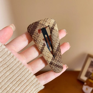 Detail of a brown houndstooth fabric triangular hair clip with a sturdy metal BB base
