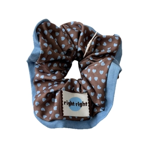 Scrunchie marrone con motivi a cuori blu ed etichetta in tessuto su sfondo bianco