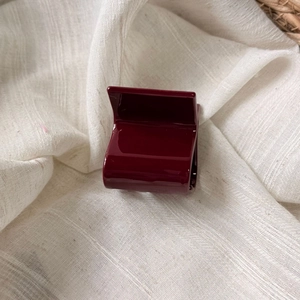 Detailed view of a small glossy wine red rectangular hair claw clip on white linen cloth