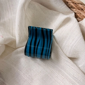 Macro shot of bright blue acetate hair claw with elegant black stripes on fabric background