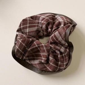 Macro detail of plaid fabric hair claw with brown leather edge and pleated texture