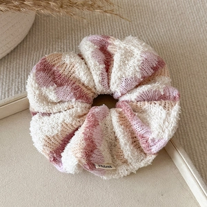Close-up of a striped knit scrunchie with soft pink, purple, and cream textured wool yarn