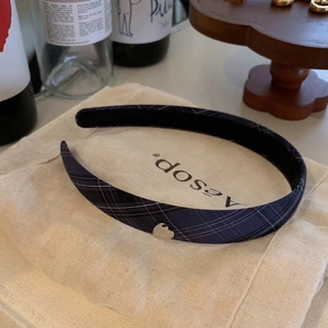 Detailed view of navy blue plaid headband with a silver heart charm on linen fabric