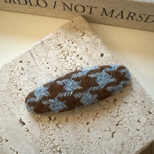 Gros plan d'une pince à cheveux en tricot à motif pied-de-poule sur support en pierre